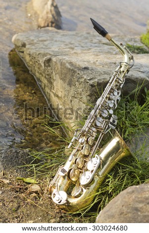 Summer Jazz saxophone in nature lying on rocks lakeside