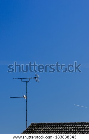 Old style TV aerial / antenna on top of black tiled roof against mainly blue sky.