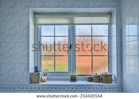 Frosted glass bathroom window with distorted orange/blue exterior, and various items on the windowsill.