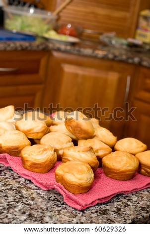 A pile of baked buns sits on a counter with out-of-focus thanksgiving meal trimmings in the background.
