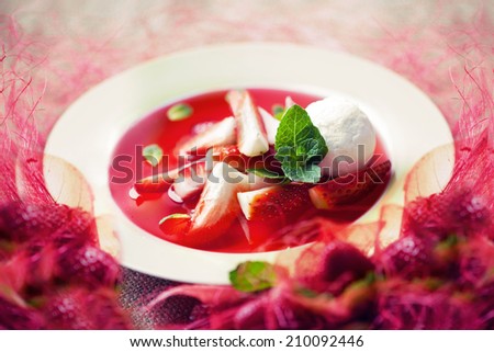 strawberry soup with ice cream and mint on a plate decorated with fresh strawberries