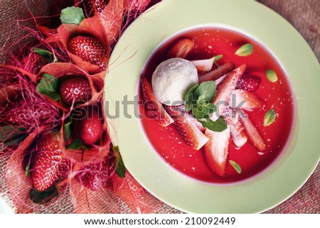 strawberry soup with ice cream and mint on a plate decorated with fresh strawberries