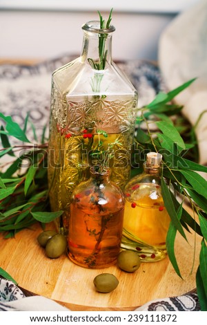 Several bottles of olive oil with rosemary and spices with olive leaves and green olives in a still life
