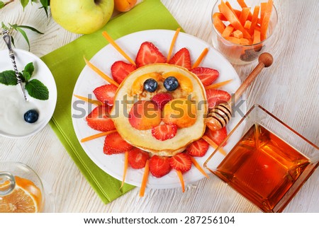 Children breakfast pancakes smiling face of the sun lion strawberry blueberry and apricot, cute food, honey, creative idea for kids