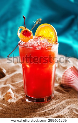 beautiful red cocktail with orange cherry ice in a still life on the sand at the ocean sea water refreshing summer beach bar