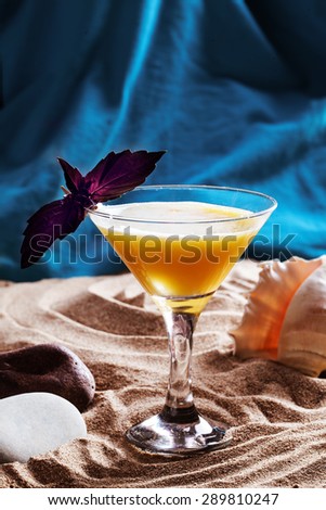 Yellow cocktail with basil on a beach sand ocean sea
