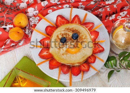 Children\'s breakfast pancakes smiling face of the sun strawberry blueberry and apricot, cute food, honey, creative idea lunch food idea meal dinner