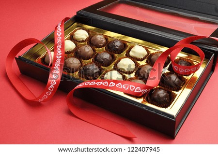 Beautiful black and gold closed box of delicious chocolates in a black and gold box with red heart ribbon on a red background, for Valentine, Christmas, birthday or Mothers Day gift.