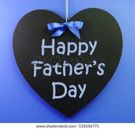 Happy Fathers Day message written on a black blackboard with blue ribbon against a blue background.