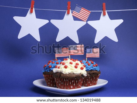 Fourth 4th of July party celebration with red, white and blue chocolate cupcakes on white heart plate and USA American flags with stars hanging from pegs on a line with copy space.