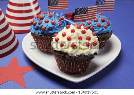Fourth 4th of July party celebration with red, white and blue chocolate cupcakes on white heart plate and USA American flags - closeup.