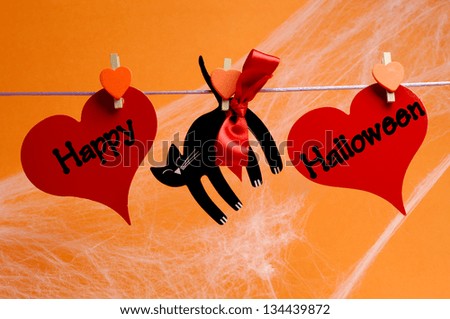Happy Halloween message written across red hearts and black cat with pegs hanging from a line against an orange background.