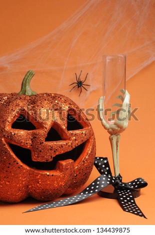 Happy Halloween Jack-o-lantern pumpkin with skeleton hand glass and polka dot ribbon with spider and web on orange background. Vertical.