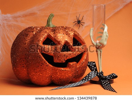 Happy Halloween Jack-o-lantern pumpkin with skeleton hand glass and polka dot ribbon with spider and web on orange background.