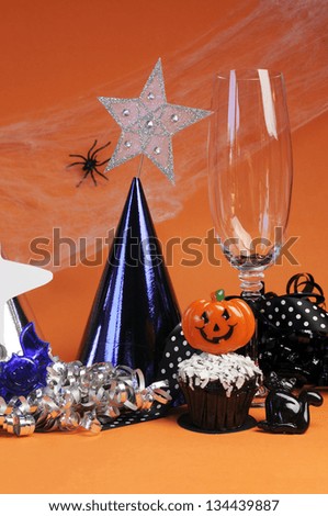 Happy Halloween party decorations with cobweb and spider, champagne glass, hats, chocolate cupcake, stars and streamers on orange background. Vertical.
