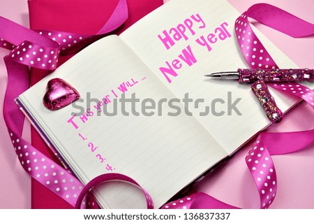 Happy New Year resolutions written in diary journal book with pretty feminine pink ribbons, heart chocolate and pen.