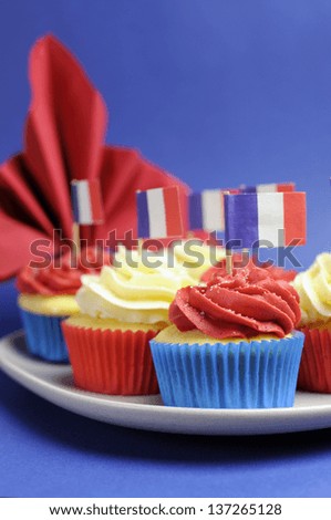 French theme red, white and blue mini cupcake cakes with flags of France and fleur-de-lis red napkin for National holidays of France, Bastille Day, the Fourteenth of July. Close up vertical.