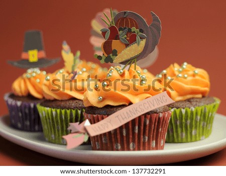Happy Thanksgiving cupcakes with turkey, feast, and pilgrim hat topper decorations against a harvest red brown background. Close up with shallow DOF bokeh.