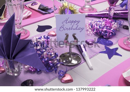 Pink and purple theme party table setting decorations with Happy Birthday message on table stand.