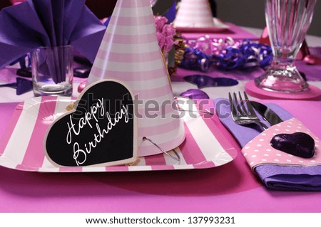 Pink and purple theme party table setting decorations with party hat closeup and Happy Birthday heart message.