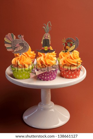 Happy Thanksgiving decorated cupcakes with turkey, pilgrim hat and corn toppers on cake stand against a brown background. Vertical