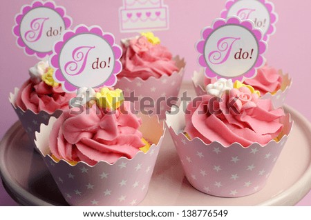 Pink wedding cupcakes with I Do topper signs on pink cake stand - close up.