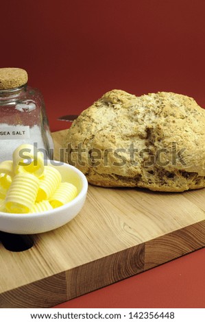 Australian traditional beer batter damper bread with butter curls on bread board against a red ochre background. Vertical with sea salt bottle.