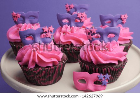 Pink and purple masquerade masks decorated party cupcakes with pink frosting for Mardi Gras, teenage, birthday, New Years Eve, or wedding bridal shower party - close up.