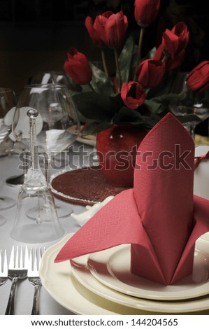 Red and white theme wedding breakfast dining table setting with red table napkins in bishop style folds, for weddings or Valentine day banquet meal. Vertical.