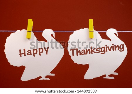 Celebrate Thanksgiving on the last Thursday in November with a Happy Thanksgiving message greeting written across white turkeys hanging from pegs on a line against a red brown background.