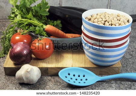 Vegetarian cooking concept with eggplant, carrots, tomatoes, and red onion with dried chick peas and blue, red and white cooking utensils for healthy diet concept or World Vegetarian Day on October 1.