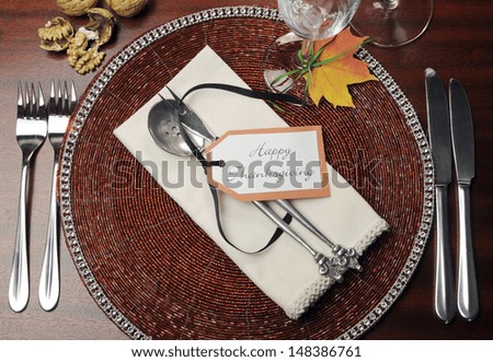 Beautiful Autumn Fall theme Thanksgiving dinner table place setting with Happy Thanksgiving tag attached to silverware. Aerial view with walnuts.