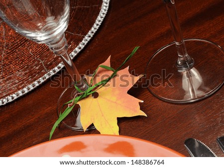 Beautiful Autumn Fall theme Thanksgiving dinner table place setting with Happy Thanksgiving tag attached to silverware. Close up on Fall Leaf glass place holder.