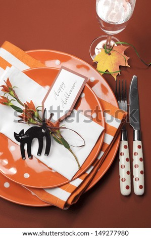 Bright and modern Happy Halloween orange polka dot and stripes plates and napkins lunch or dinner table setting. Aerial vertical.
