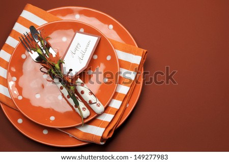 Bright and modern Happy Halloween orange polka dot and stripes plates and napkins lunch or dinner table setting, with copy space for your text here.