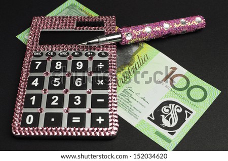 Savings and money management concept with Australian dollar notes, pink calculator and piggy bank against a black background.