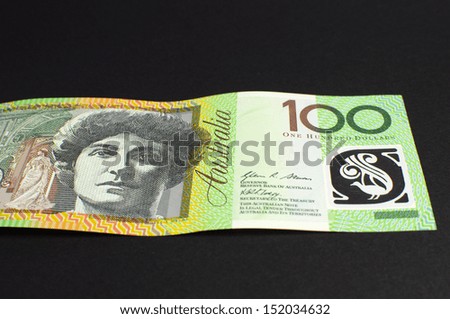Australian green and gold  100 hundred dollar note, against a black background, laying flat.