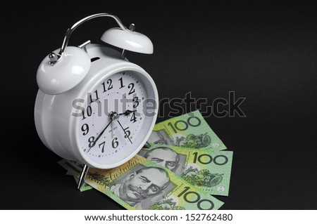 White old fashion alarm clock with Australian hundred dollar notes on black background for time and money concept.