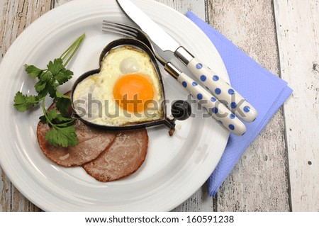 Modern high protein breakfast of ham with heart shape egg cooked breakfast on vintage shabby chic blue table with polka dot cutlery.