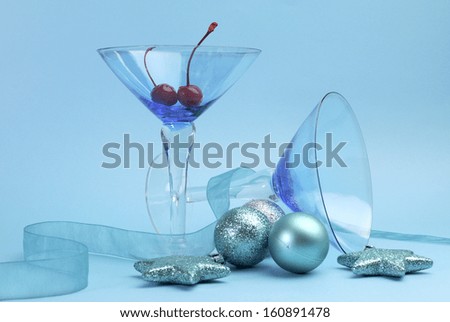 Festive spirit blue martini cocktail glasses with red maraschino cherries and christmas baubles on an aqua blue background. Vertical.