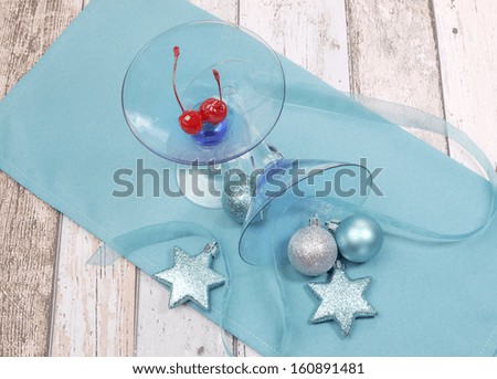 Festive spirit blue martini cocktail glasses with red maraschino cherries and christmas baubles on a shabby chic table