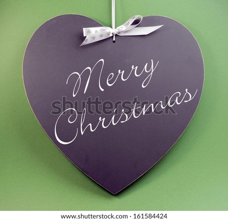 Merry Christmas message greeting written on heart shape blackboard sign on green background.