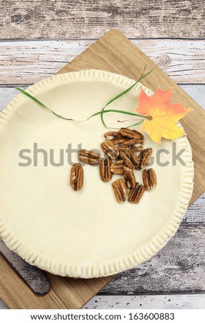 Holiday festive baking with an empty pie shell pastry crust with raw pecan nuts ingredients and autumn leaf decoration.