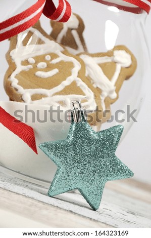 Merry Christmas gingerbread santa and snowman cookies in a festive glass cookie jar with white icing frosting on blue and white shabby chic table with white background. Close up.