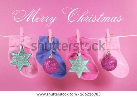 Festive childrens baby stockings hanging from pegs on a line with Merry Christmas greeting and ornaments decorations against a pretty pink background. Baby\'s First Christmas or Young Family greeting.