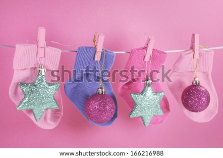 Festive childrens baby stockings hanging from pegs on a line with Merry Christmas greeting and ornaments decorations against a pretty pink background. Baby\'s First Christmas or Young Family greeting.