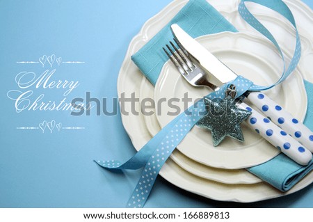 Aqua blue Merry Christmas dining table place setting with fine china and polka dot cutlery on blue background with copy space.