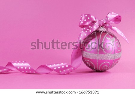 Beautiful fuchsia pink festive bauble ornament with polka dot ribbon on a feminine pink background with copy space for Merry Christmas or Happy Holidays seasons greetings.