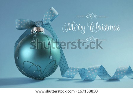 Close up of beautiful aqua blue Christmas tree ornament with polka dot ribbon, backlit with Merry Christmas text greeting.