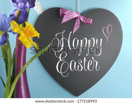 Happy Easter greeting on heart shape blackboard or copy space with spring flowers in pink vase on blue background.